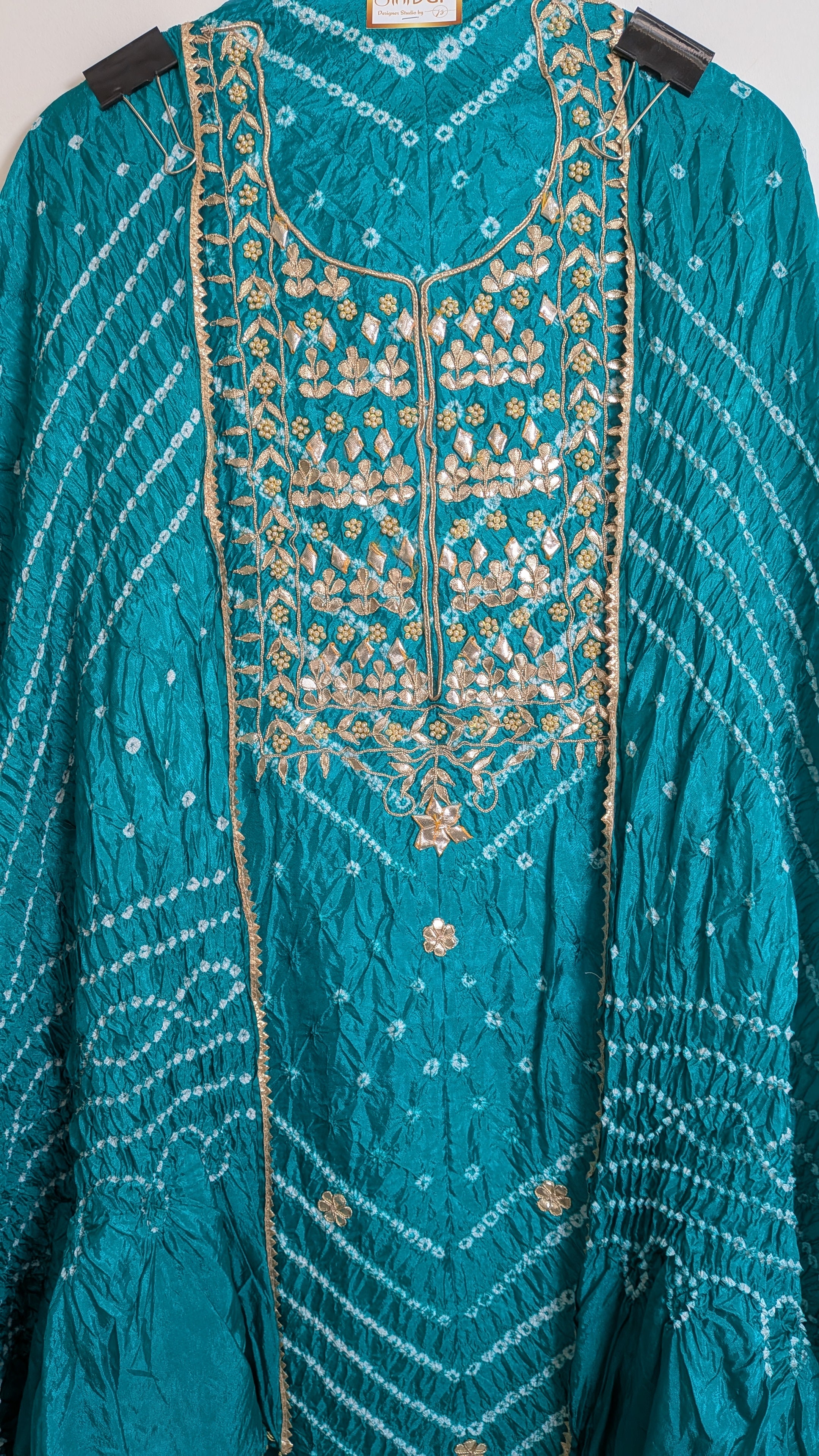 Teal embroidered garment with gold details on a hanger