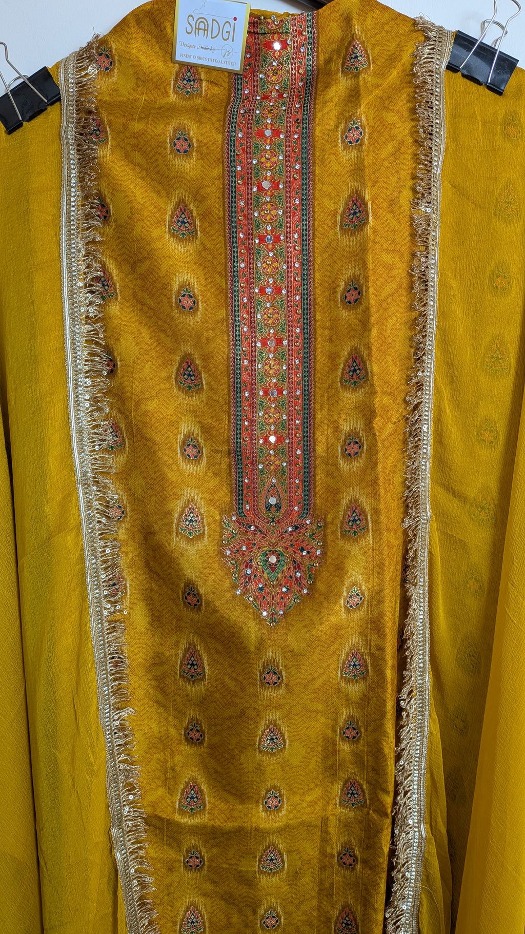 Mustard yellow traditional outfit with intricate embroidery on a hanger.