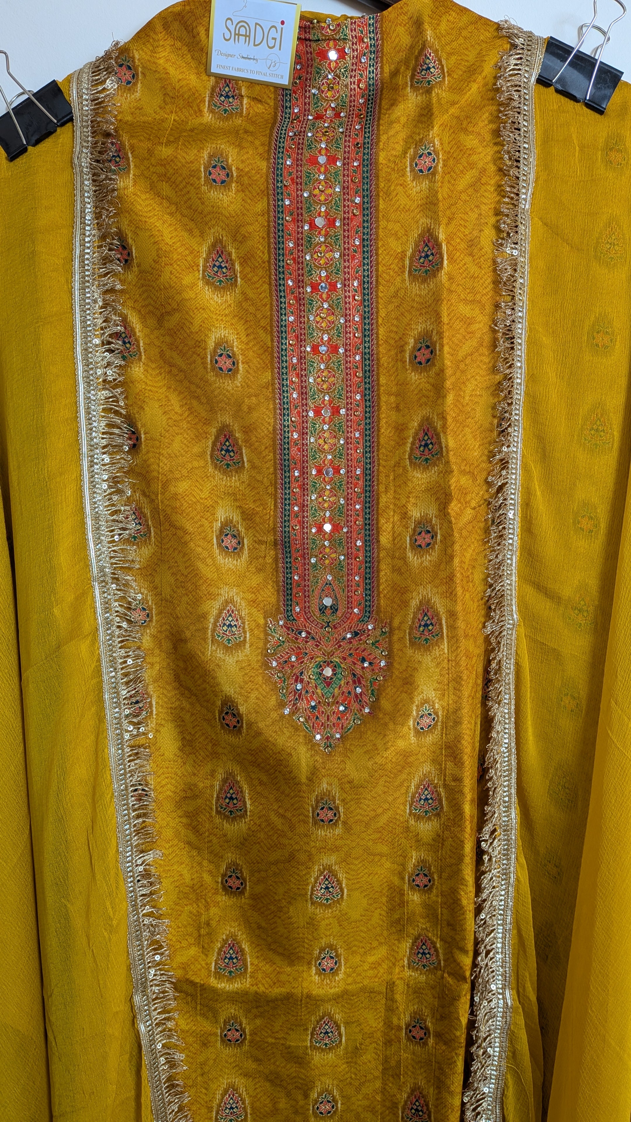 Mustard yellow traditional outfit with intricate embroidery on a hanger.