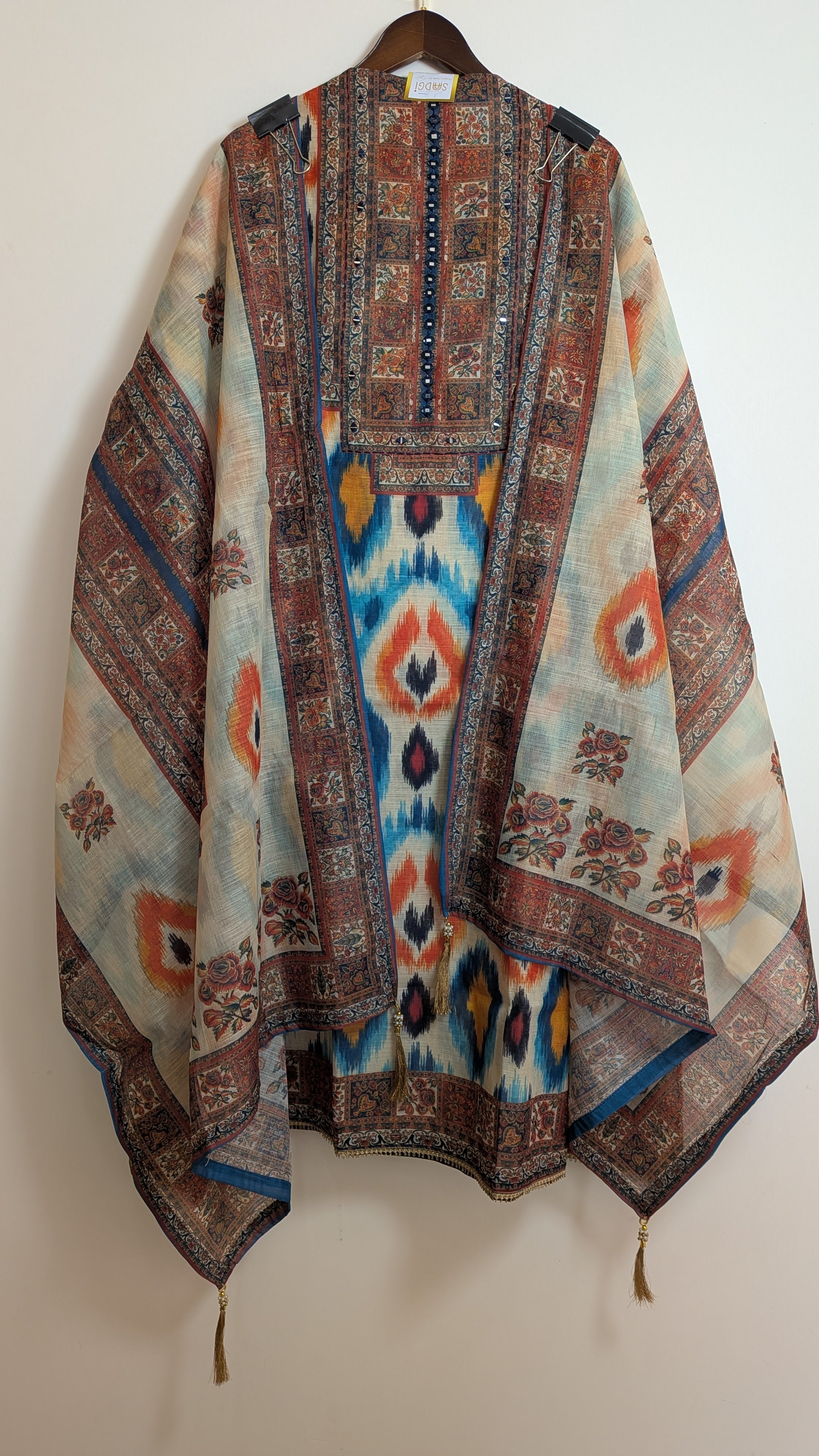 Colorful patterned shawl on a hanger against a white background