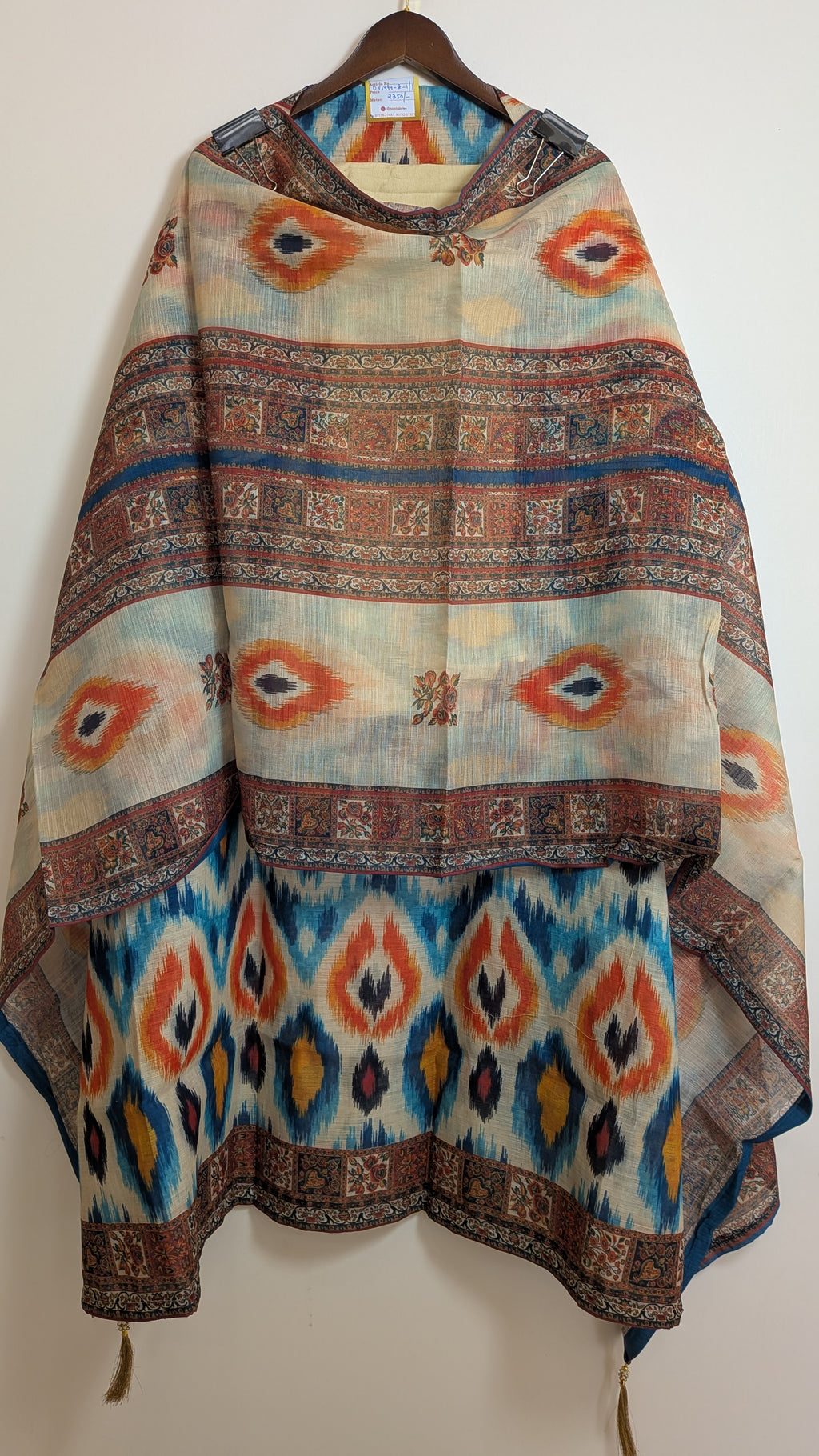 Colorful patterned shawl on a wooden hanger against a white wall