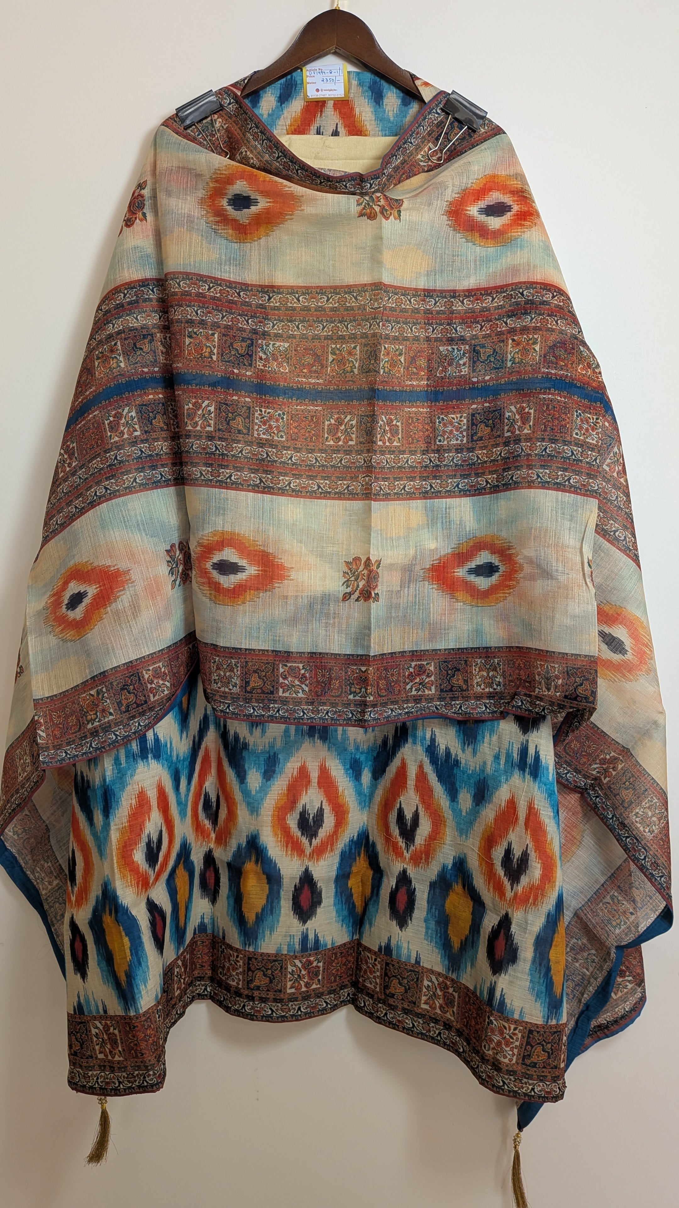 Colorful patterned shawl on a wooden hanger against a white wall